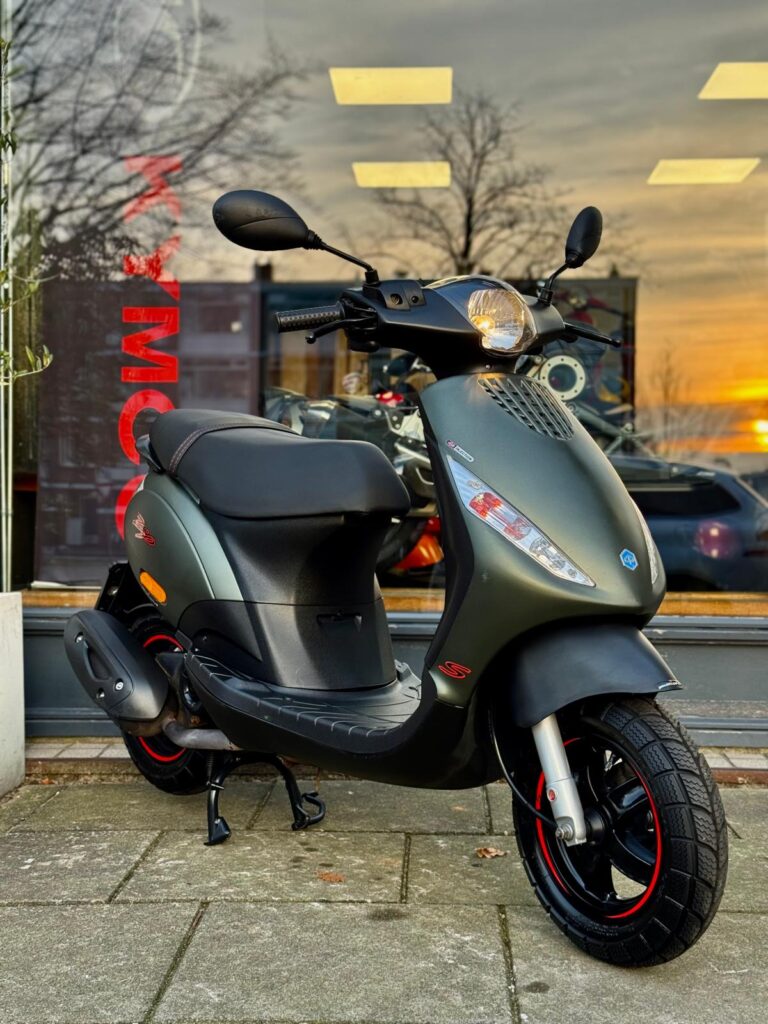 Matgroene scooter op standaard voor een winkelraam, met zonsondergang weerspiegeld in het glas.
