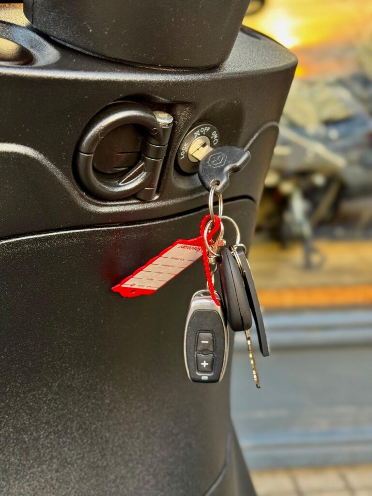 Close-up van een scooterslot met sleutelbos en zwarte afstandsbediening.
