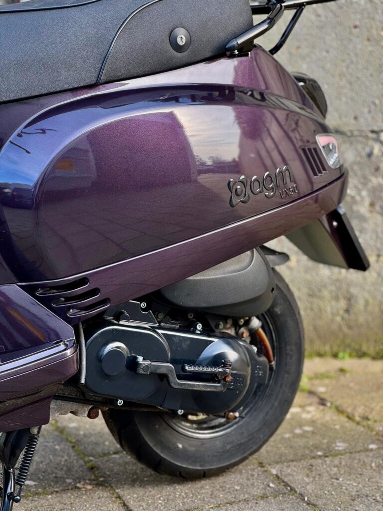 Close-up van paarse AGM VX50 scooter, achterzijde met achterwiel en motor bij stoep.