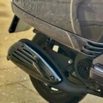 Close-up van de uitlaat en het achterwiel van een AGM VX50 scooter op de stoep.