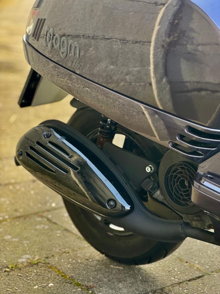 Close-up van de uitlaat en het achterwiel van een AGM VX50 scooter op de stoep.