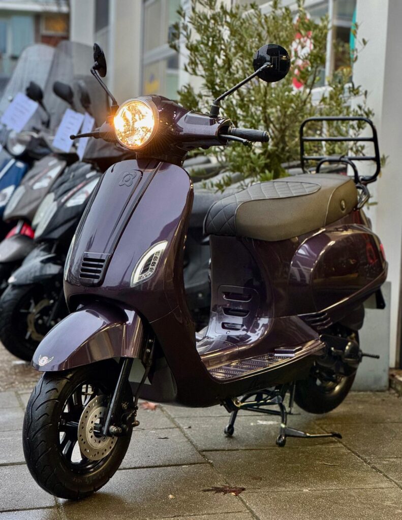 Paarse retro scooter met brandende koplamp op nat trottoir voor een winkel.