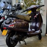 Donkerpaarse retro-scooter op de standaard met achterdrager, voor een winkel met andere scooters.