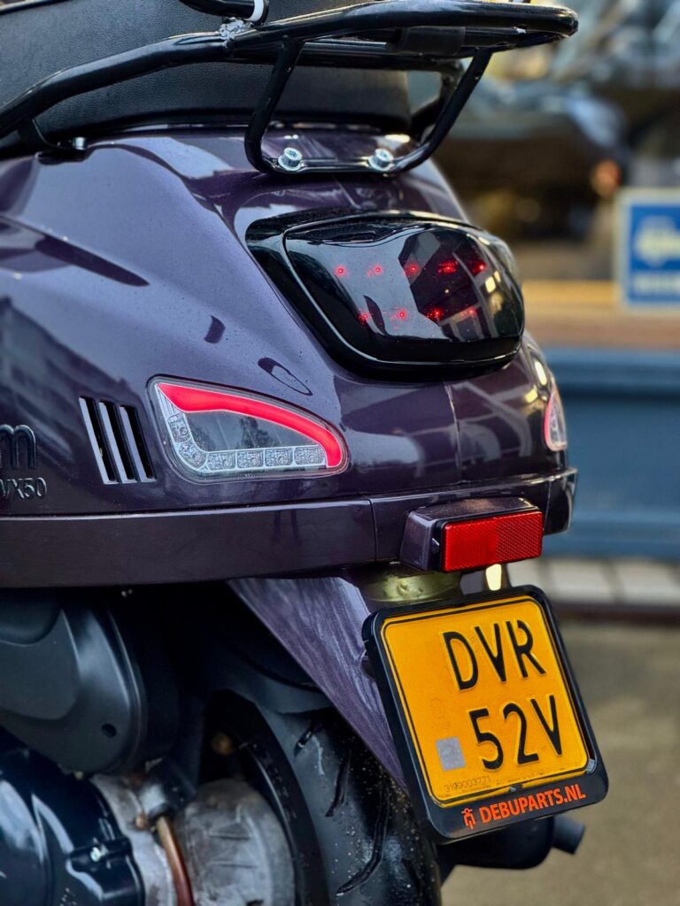 Achterzijde van paarse scooter met achterlicht, bagagedrager en gele kentekenplaat
