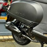 Close-up van de achterzijde van een matte zwarte La Souris scooter met uitlaat en wiel.