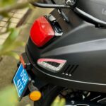 Close-up van de achterzijde van een matzwarte scooter met rood achterlicht en blauwe kentekenplaat.