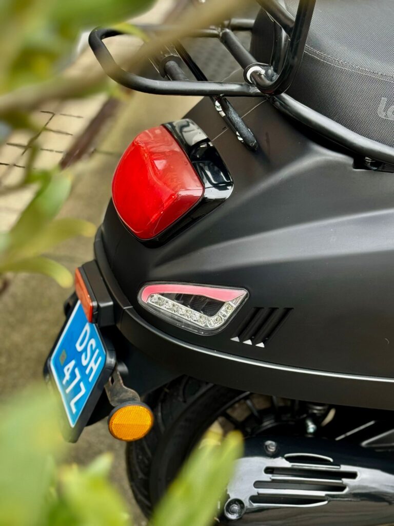 Close-up van de achterzijde van een matzwarte scooter met rood achterlicht en blauwe kentekenplaat.
