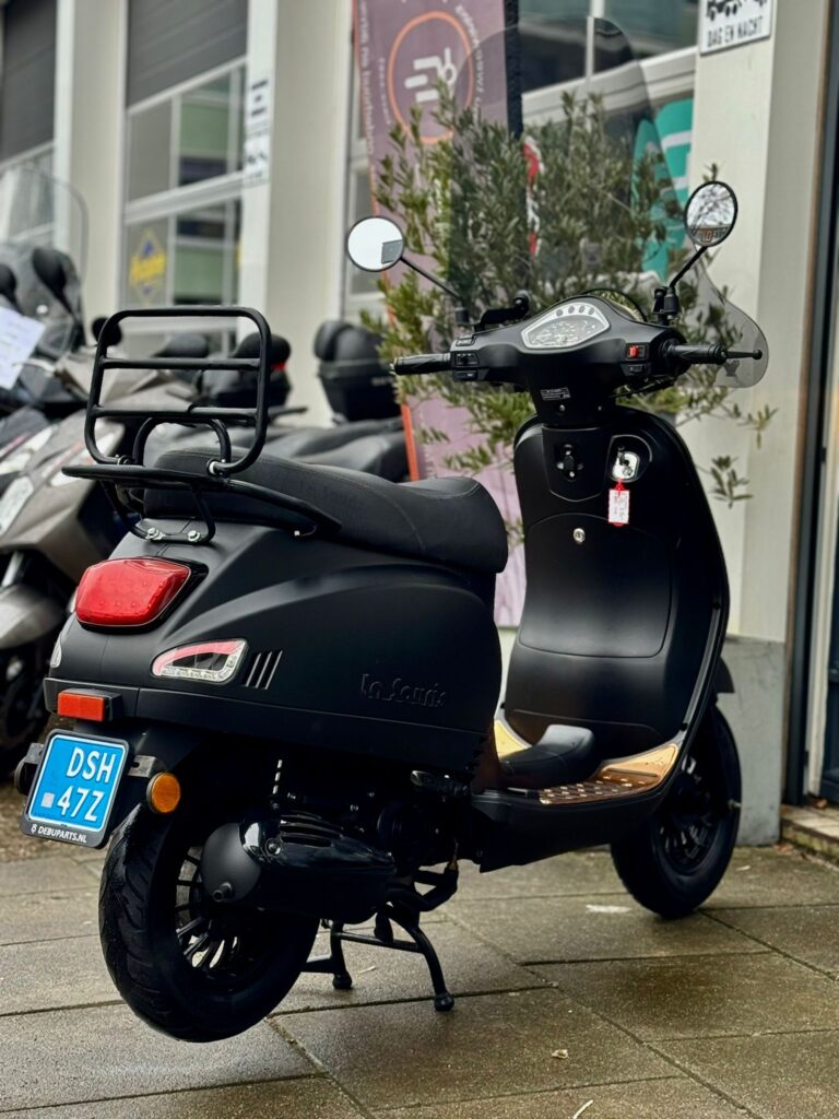 Matzwart retro-scooter met bagagedrager en blauwe kentekenplaat, geparkeerd voor een scootershop.