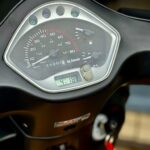 Close-up van een scooterdashboard met snelheidsmeter, brandstof- en temperatuurmeter en klein digitaal klokje.