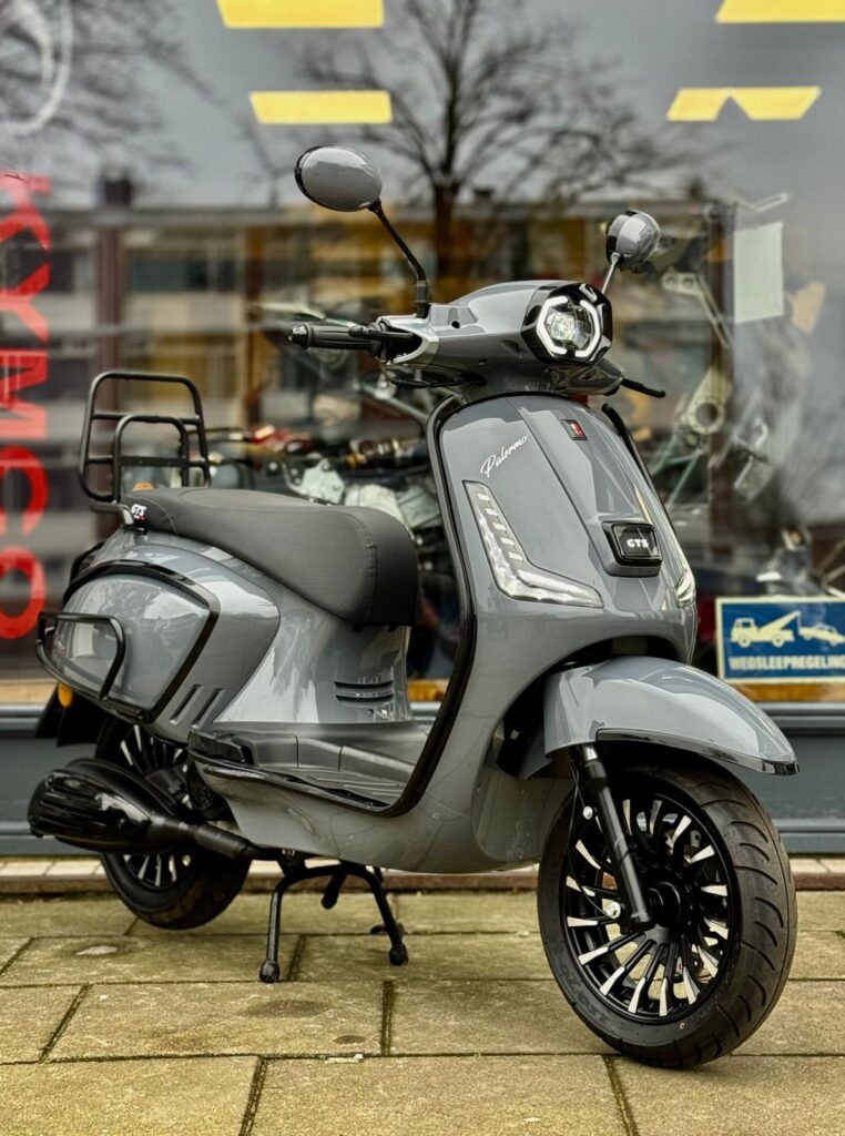 Grijze retro-stijl scooter met LED-verlichting, geparkeerd voor een etalage op de stoep.