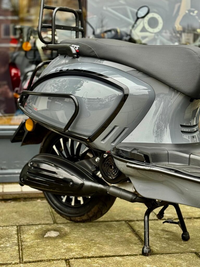 Close-up van de zijkant van een grijze scooter op de middenbok, met uitlaat, wiel en bagagedrager.