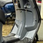 Detail van een grijze scooter met contactsleutel in het contact en rubberen voetplaat.