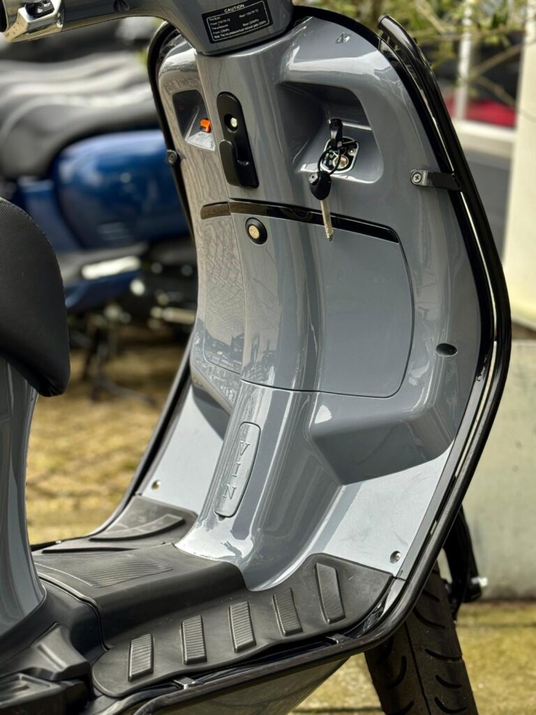 Detail van een grijze scooter met contactsleutel in het contact en rubberen voetplaat.