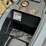 Opbergvak onder het zadel van een scooter met tankdop, waarschuwingstickers en service-label.