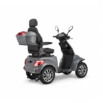 Grijze vierwielige scootmobiel met hoge rugleuning, armsteunen en topkoffer, driekwart achteraanzicht.