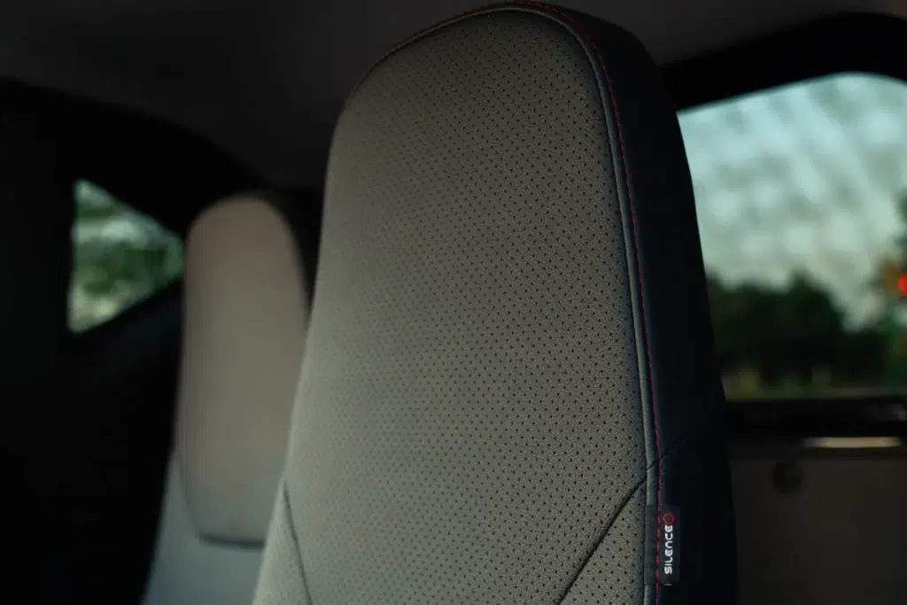 Close-up van een geperforeerde autostoelhoofdsteun met rode stiksels en Silence-label.
