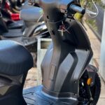 Close-up van het stuur, dashboard en voetplaat van een zwarte scooter met sleutel, geparkeerd buiten.