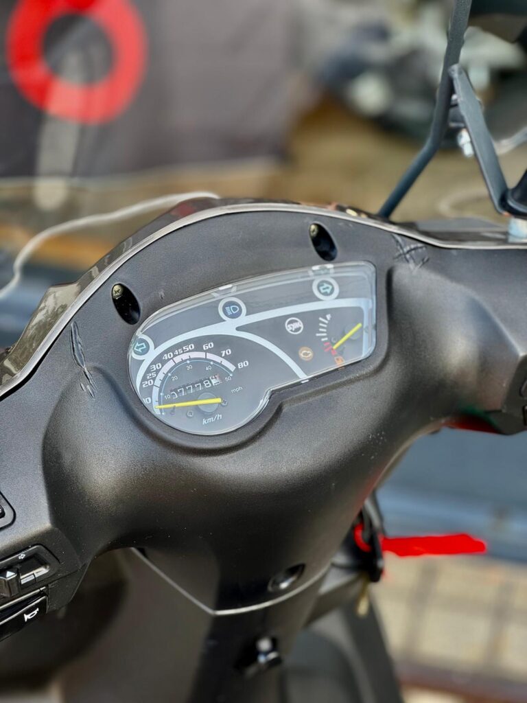 Close-up van het dashboard van een scooter met analoge snelheidsmeter en kilometerteller.