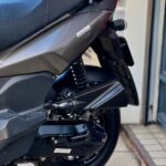 Close-up van de achterzijde van een grijze scooter met zadel, veer en achterwiel op de stoep.