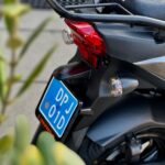 Achterkant van een zwarte SYM-scooter met bagagedrager, achterlicht en blauwe kentekenplaat.