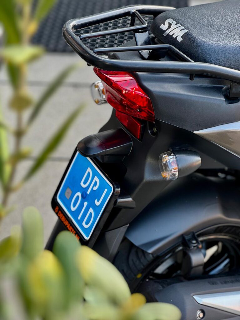 Achterkant van een zwarte SYM-scooter met bagagedrager, achterlicht en blauwe kentekenplaat.