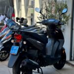 Zwarte scooter op standaard voor een winkel, met andere scooters op de achtergrond.