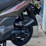 Close-up van de achterzijde van een grijze scooter met wiel, veer en uitlaat op de stoep.