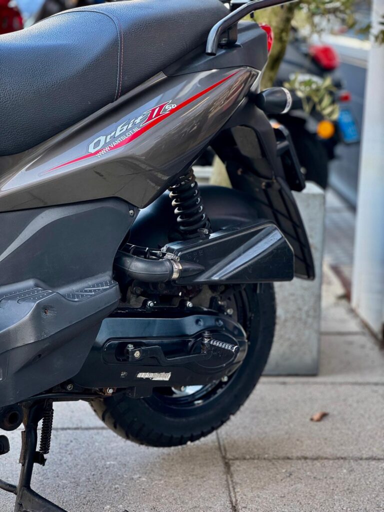 Close-up van de achterzijde van een grijze scooter met wiel, veer en uitlaat op de stoep.