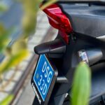 Close-up van de achterkant van een zwarte scooter met blauwe kentekenplaat en rood achterlicht.