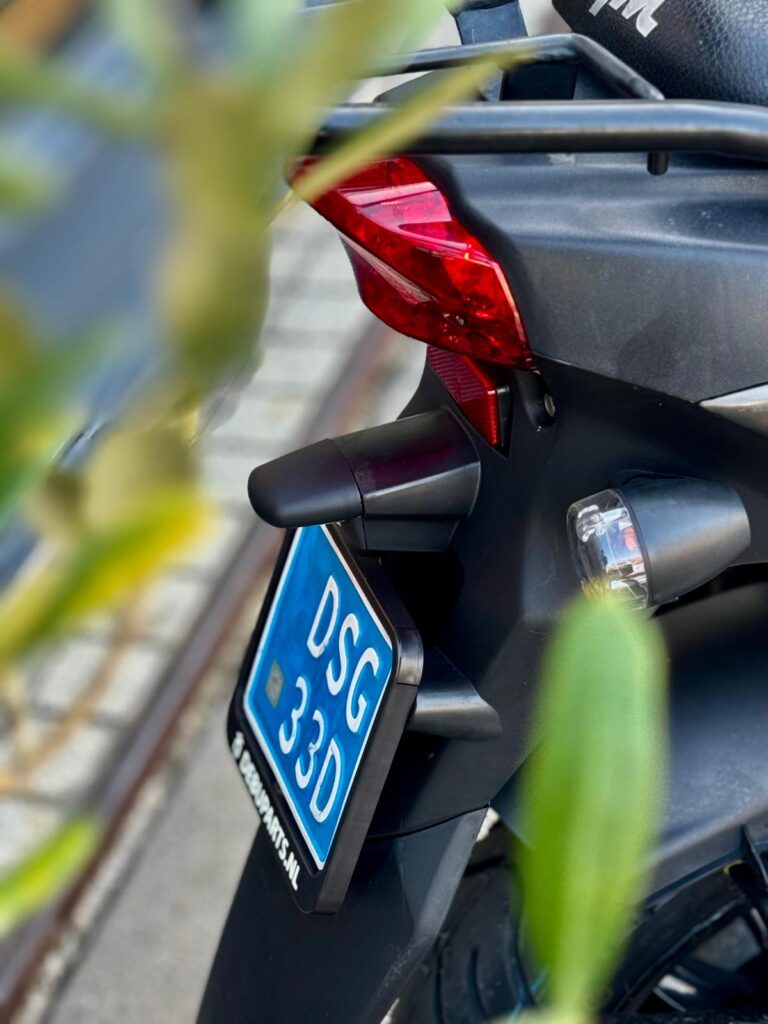 Close-up van de achterkant van een zwarte scooter met blauwe kentekenplaat en rood achterlicht.