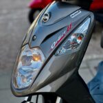 Close-up van de voorkant van een grijze SYM Orbit II scooter met koplampen.