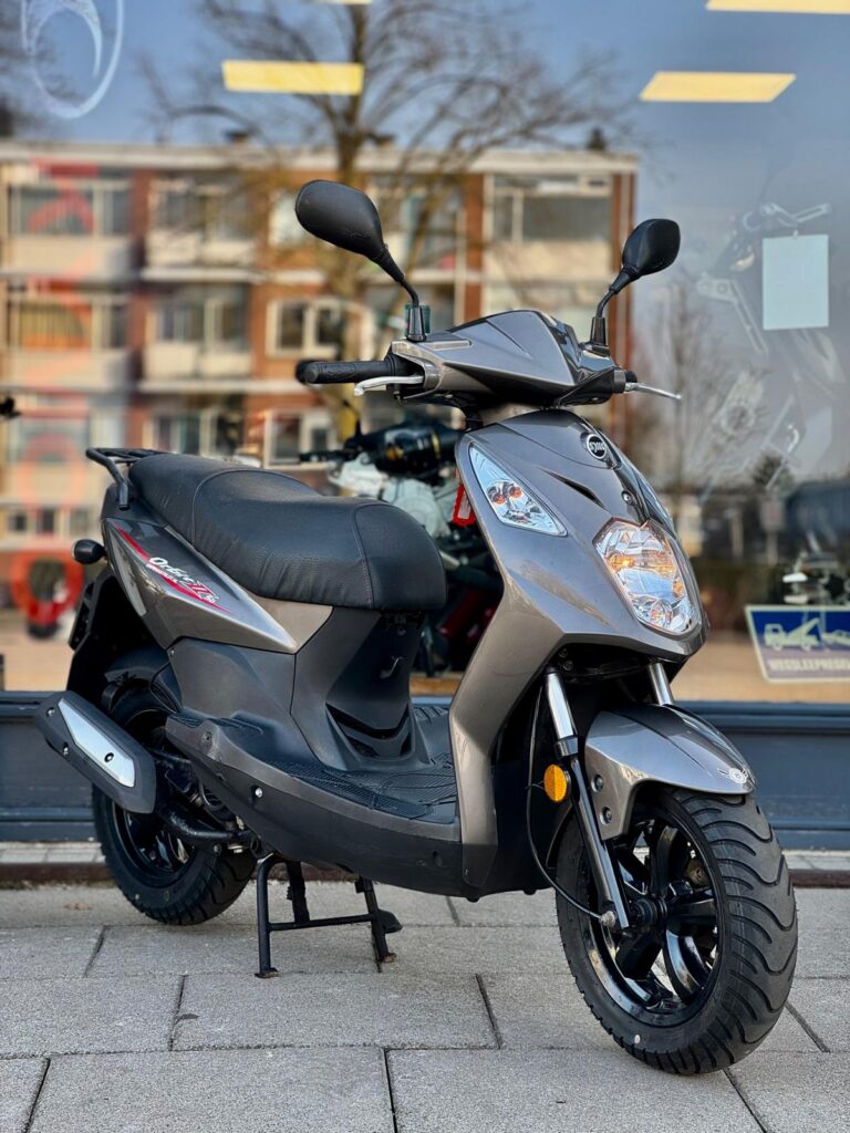 Grijze scooter op standaard voor een winkelraam, met flats weerspiegeld op de achtergrond.