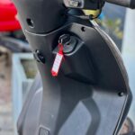 Close-up van het stuur en dashboard van een scooter met sleutel en rood label in het contactslot.