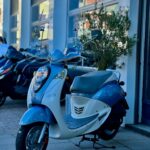 Lichtblauwe retro-scooter op standaard voor een showroom, met andere scooters op de achtergrond.