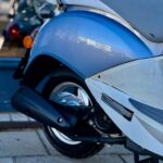 Close-up van de achterkant van een lichtblauwe scooter met grijze zitting en uitlaat op de stoep.