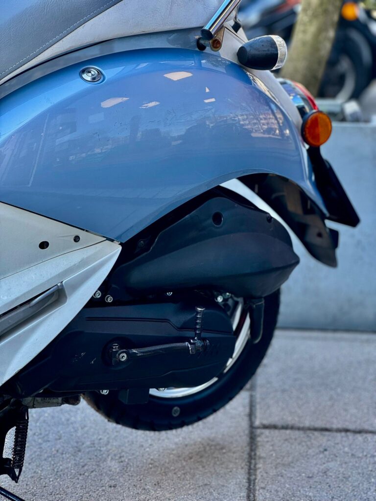 Close-up van het achterwiel en spatbord van een blauwe scooter met knipperlicht.