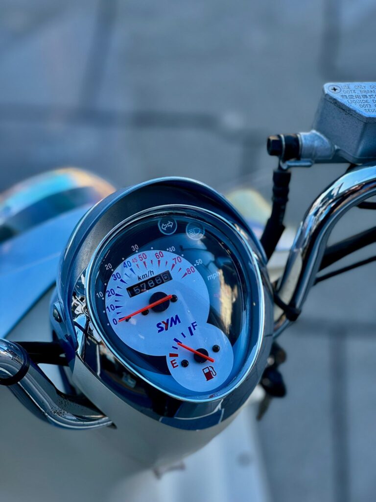 Close-up van het dashboard van een SYM-scooter met snelheidsmeter en brandstofmeter.
