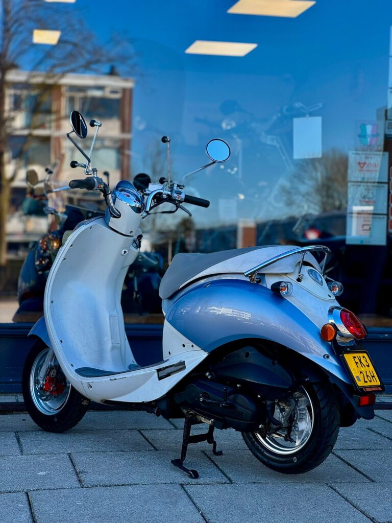 Blauw-witte retro scooter geparkeerd op trottoir voor winkelruit met reflecties.