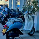 Lichtblauwe en witte retro scooter geparkeerd voor een rij scooters bij een showroom