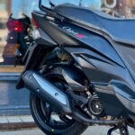 Close-up van de achterzijde van een zwarte scooter op de middenstandaard, model Orbit III, bij een winkelruit.