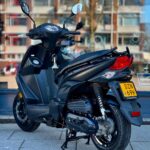 Matzwarte scooter op de stoep, op de middenbok, voor een etalage met woonflats.