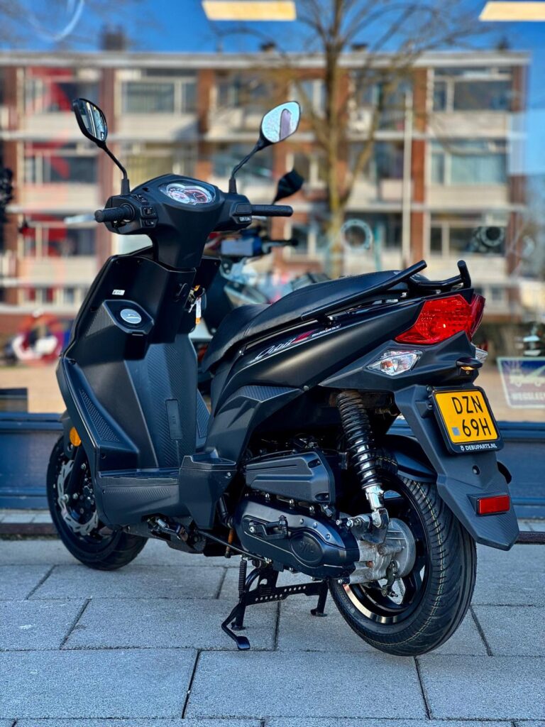 Matzwarte scooter op de stoep, op de middenbok, voor een etalage met woonflats.