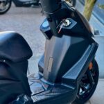 Close-up van een zwarte scooter met sleutel in het contact, gezien bij stuur en voetplaat op straat.