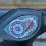 Close-up van een scooterdashboard met snelheidsmeter, kilometerteller en lage brandstofindicator.