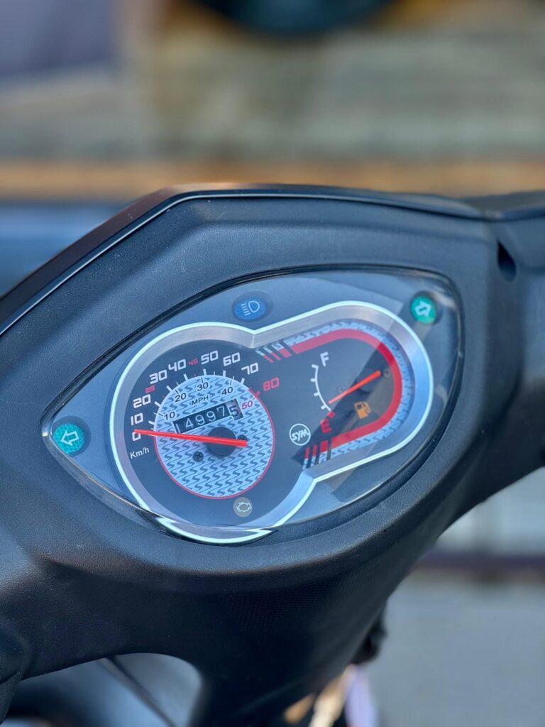 Close-up van een scooterdashboard met snelheidsmeter, kilometerteller en lage brandstofindicator.