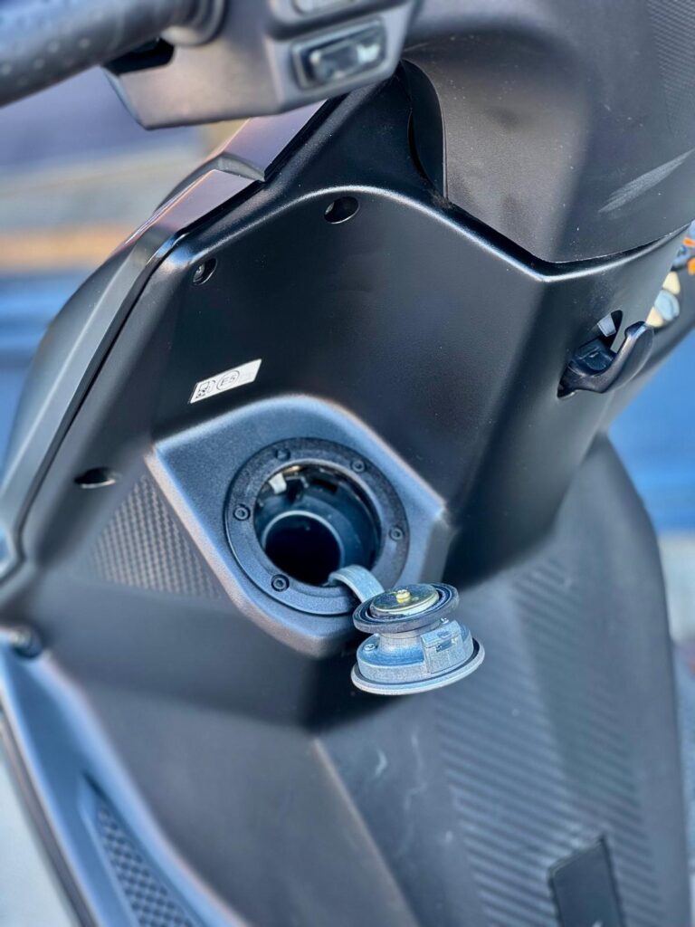 Close-up van een scooter met open brandstofdop aan de voorkant van de kuip.