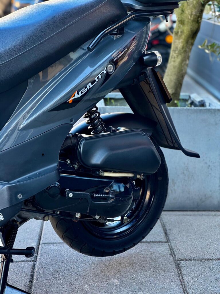 Detail van de achterzijde van een grijze Kymco Agility scooter met achterwiel en vering.