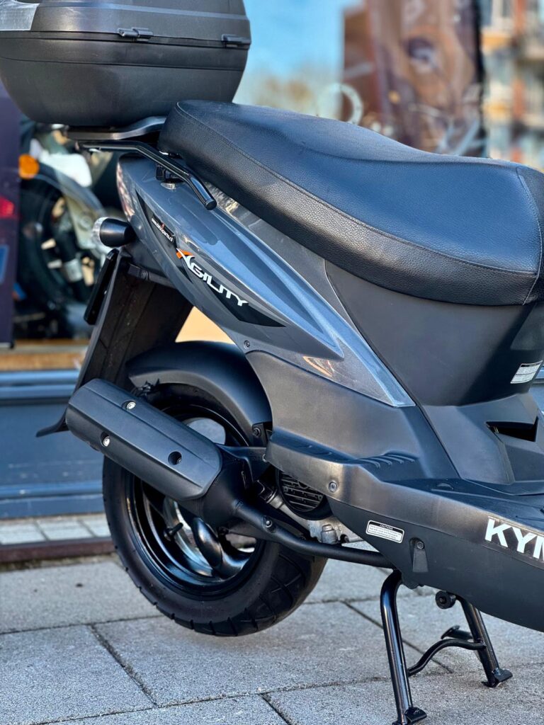 Close-up van de achterkant van een grijze Kymco Agility-scooter op de middenbok met topkoffer.