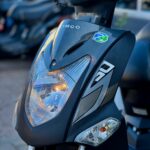 Close-up van de voorkant van een grijze Kymco-scooter met brandend koplampje.