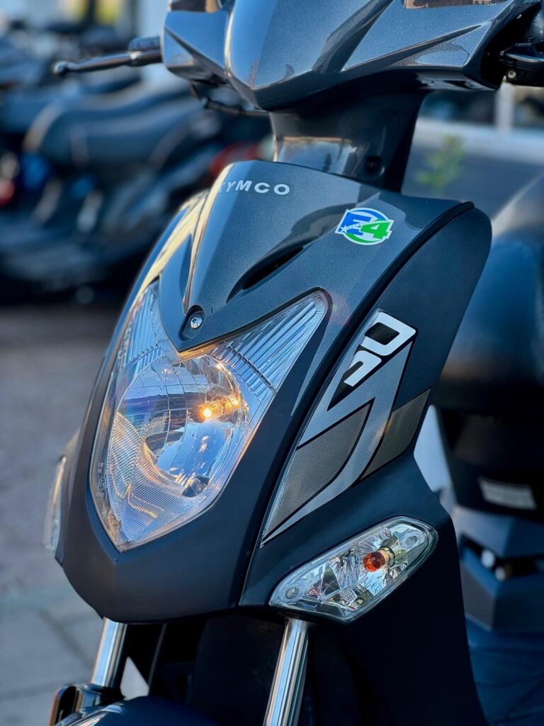 Close-up van de voorkant van een grijze Kymco-scooter met brandend koplampje.